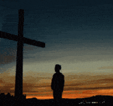 a silhouette of a person standing in front of a cross at sunset