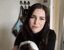 a woman holds a cat in her arms in front of a wall with hooks on it
