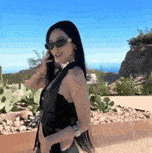 a woman wearing sunglasses and a choker stands in front of a cactus