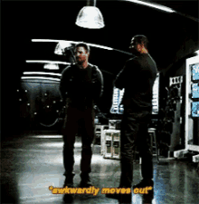 two men are standing next to each other in a dark room and one of them is saying " awkwardly moves out "