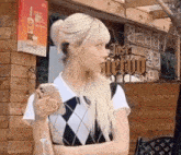 a woman with blonde hair is standing in front of a building holding a cell phone .
