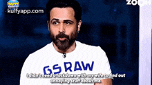 a man with a beard wearing a gs raw shirt is talking on a video call .