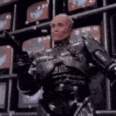 a man in a robot suit is standing in front of a wall of televisions holding a gun .