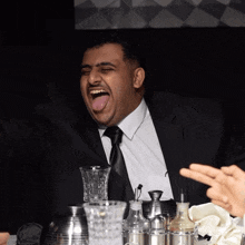 a man in a suit and tie is sitting at a table with his tongue out