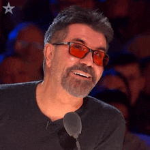 a man wearing red glasses is smiling in front of a microphone with a star in the background
