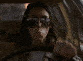 a woman wearing sunglasses is blowing a pink bubble while driving a car