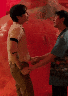 two men are hugging each other in front of a red background with the letter t on it