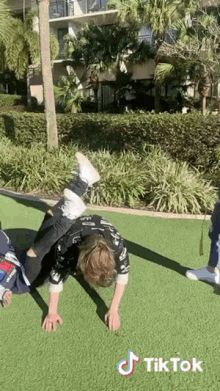 a young boy is doing a handstand on a grassy field with a tiktok logo in the corner