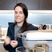 a woman is standing in front of a mixer and making a face