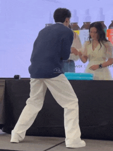 a man in a blue jacket is dancing in front of a woman in a white dress with the number 16 on the back