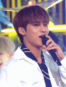 a man is singing into a microphone while wearing a white shirt and tie .