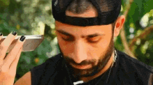 a man with a beard wearing a hat is holding a cell phone to his face