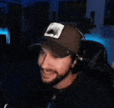 a man with a beard wearing a hat and headphones is sitting in front of a microphone .