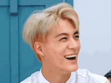 a young man with blonde hair and a white shirt is smiling .