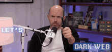 a man is sitting in front of a microphone with the words let 's dark web behind him .