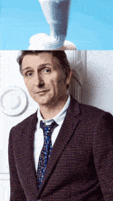 a man in a suit and tie stands in front of a white wall