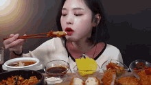 a woman is eating fried food with chopsticks while sitting at a table with bowls of food .