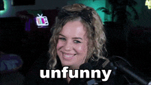 a woman with a cat ear headband smiles in front of a microphone with the word unfunny behind her