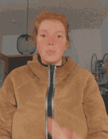 a woman with red hair is wearing a brown jacket and making a funny face .