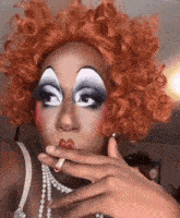 a drag queen is wearing a wig and smoking a cigarette .