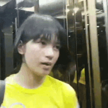 a girl wearing a yellow shirt is standing in an elevator .