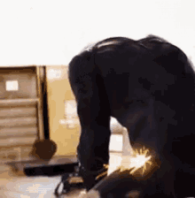a man is kneeling down on the floor cutting a piece of metal with a grinder .