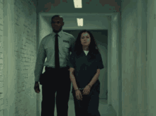 a woman in handcuffs is walking down a hallway with a man
