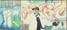 a man wearing sunglasses is standing in front of a wall with graffiti on it that says jc on it