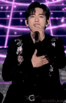 a young man is singing into a microphone while wearing a floral jacket .