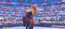 two women are wrestling in a wrestling ring with a referee in front of a crowd .
