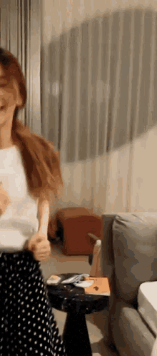 a woman in a polka dot skirt is dancing in a living room next to a table .