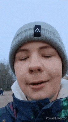 a young man wearing a gray beanie and a blue jacket is making a funny face .