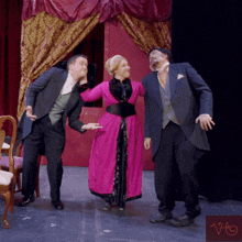 a woman in a pink dress stands between two men