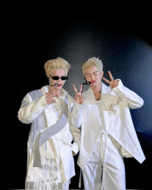 two men wearing white jackets and sunglasses are giving the peace sign