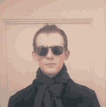 a young man wearing sunglasses and a scarf looks at the camera