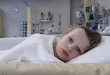 a young boy is laying in a hospital bed with a white blanket on him