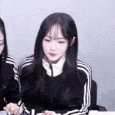a girl wearing a black jacket with white stripes on the sleeves