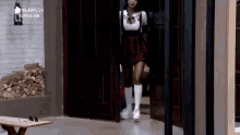 a woman in a plaid skirt and white knee high socks is walking through a door .