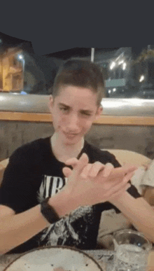 a young man is sitting at a table with his hands together and making a funny face .
