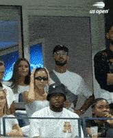 a group of people are watching a tennis match sponsored by us open .