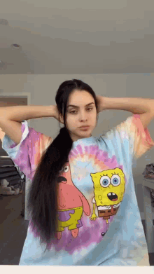 a woman wearing a tie dye shirt with spongebob and patrick on it is holding her hair in a ponytail .