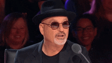 a man wearing a hat and sunglasses is speaking into a microphone