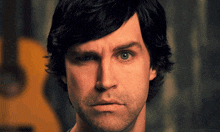 a close up of a man 's face with a yellow guitar behind him