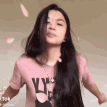 a woman with long black hair is wearing a pink t-shirt and a necklace .