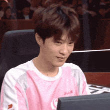 a young man wearing a pink and white shirt with the letter g on it is sitting in front of a computer monitor