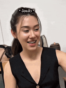 a woman wearing a black tank top smiles with a foreign language sticker on her head