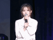a woman in a white shirt holds a microphone in front of her face