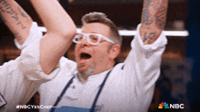a chef is celebrating with his arms in the air with the nbc logo in the background