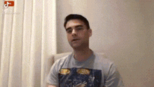 a man in a t-shirt is sitting in a chair in front of a white wall .