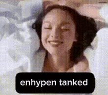 a woman is smiling with her eyes closed and a sign that says enhypen tanked .